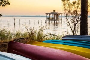 A photograph to represent Alabama, featuring a gazebo on a lake with colorful kayaks in the foreground.