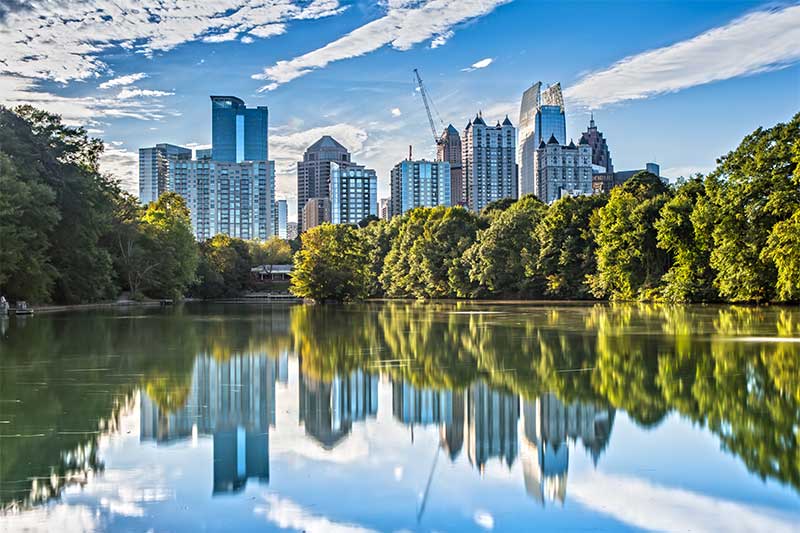 A photograph to represent Georgia, featuring the Atlanta skyline against a sunny blue sky with occasional clouds viewed from across a lake.