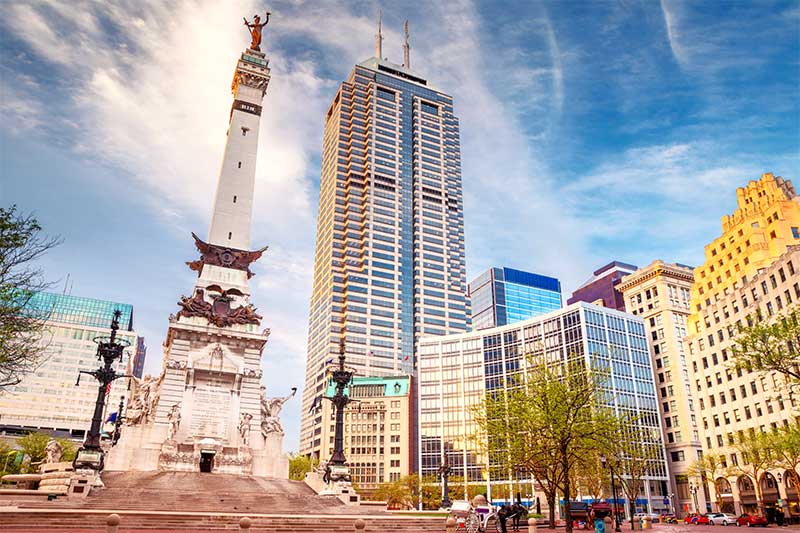 A photograph to represent Indiana, featuring the Indianapolis town square viewed from a low angle looking up at the buildings and central monument.