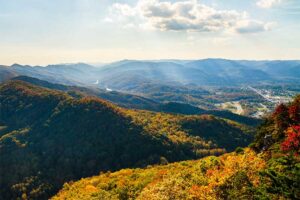 A photograph to represent Kentucky, featuring a view from a mountainside out across a valley blanketed by a dense population of red, green, and yellow deciduous trees.