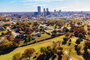 A photograph to represent Oklahoma, featuring skyscrapers in the background surrounded by large, flat, grassy areas dotted with houses.